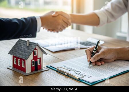 L'image montre la signature d'un contrat hypothécaire, avec une maison symbolisant l'achat. Deux bras se serrent la main, scellant l'accord formel à acqui Banque D'Images