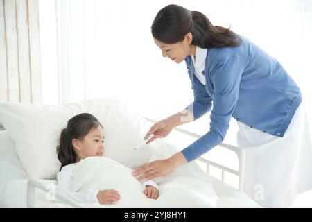 Infirmière qui remet un thermomètre à une fille dans un lit d'hôpital Banque D'Images