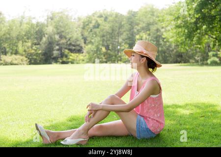 Femme dans le chapeau de paille assis à l'ombre sur la pelouse Banque D'Images