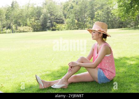 Femme dans le chapeau de paille assis à l'ombre sur la pelouse Banque D'Images