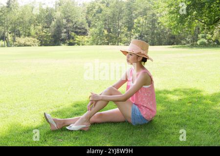 Femme dans le chapeau de paille assis à l'ombre sur la pelouse Banque D'Images