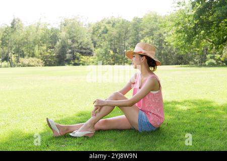 Femme dans le chapeau de paille assis à l'ombre sur la pelouse Banque D'Images