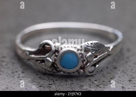 Gros plan de la bague amérindienne turquoise argentée sur le comptoir en granit. Petite pierre bleue. Banque D'Images