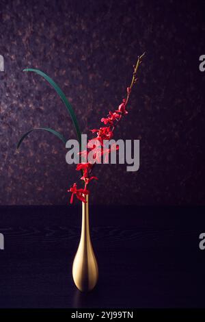 Fleurs rouges et feuilles minces dans un vase doré Banque D'Images