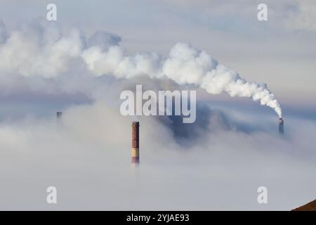 De la fumée s'écoule des cheminées industrielles masquées par le brouillard dans une région éloignée au petit matin Banque D'Images