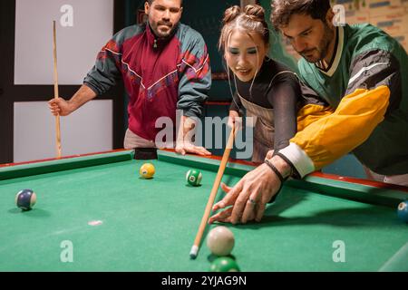Trois jeunes amis divers s'amusant tout en jouant au billard ensemble au bar des sports branché lors d'une soirée décontractée Banque D'Images