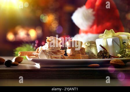 Assiette avec des morceaux de nougat fraîchement préparé sur une table en bois avec des décorations de Noël et chapeau de Père Noël avec un fond accueillant d'un roo de salle à manger Banque D'Images