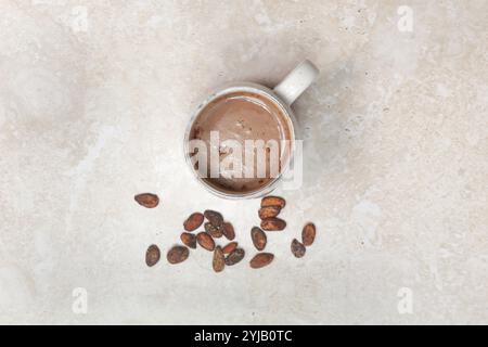Boisson chaude au cacao dans une tasse en céramique avec des fèves de cacao autour, vue d'en haut Banque D'Images