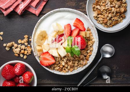Bol de granola avec yaourt grec, fraises et tranches de banane sur un fond en bois, vue de dessus de table d'un délicieux petit déjeuner sain ou d'une collation Banque D'Images