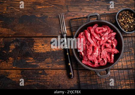Tranches de viande de boeuf crue pour stroganoff de boeuf dans une poêle. fond en bois. vue de dessus Banque D'Images