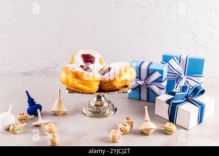 Beignets festifs sur un plateau d'argent parmi les boîtes avec des cadeaux pour les vacances Hanukkah. dreidels tétraédriques en bois. Le concept de Hanukkah. Banque D'Images