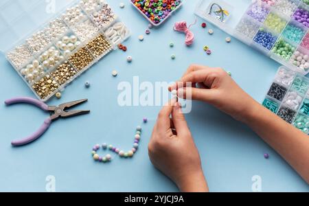 Une personne enfile habilement des perles sur une ficelle, entourée de divers récipients de perles colorées et d'outils sur une table d'artisanat lumineuse. Banque D'Images