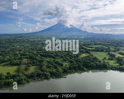 Vue aérienne époustouflante présentant un volcan entouré de champs verdoyants et d'un lac serein. Banque D'Images