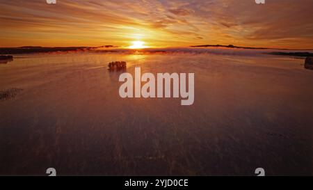 Lac, humeur matinale, coloration rouge intense dans le ciel et dans l'eau, voile de brume au-dessus de l'eau, île couverte d'arbres dans le lac, tir de drone, Lapla Banque D'Images