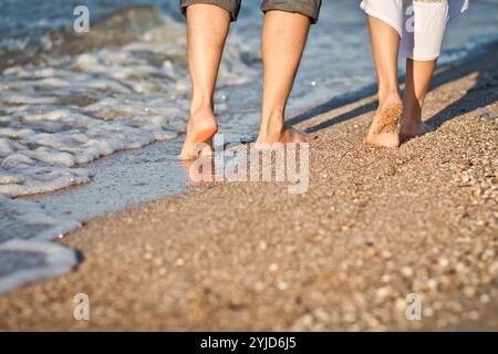 Les pieds des femmes et des hommes sur le rivage de la plage de sable par une journée ensoleillée. Marcher pieds nus. Homme et femme marchent le long du rivage, laissant des empreintes. Banque D'Images