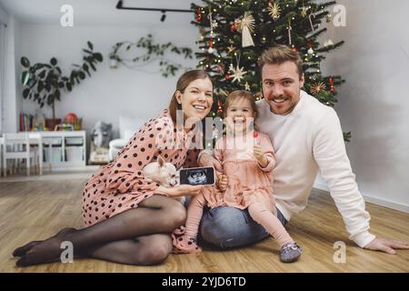 Beau portrait de Noël de la jeune famille caucasienne. Maman, papa et une petite fille. Maman et fille portant des robes roses, papa portant un pull blanc. A Banque D'Images