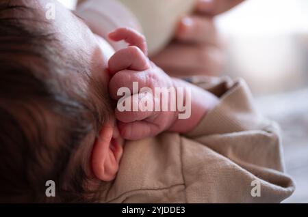 Nouveau-né nourri à partir d'un biberon, avec sa petite main à côté de la tête sous l'oreille. Boire un bébé. Scène tranquille, vue de derrière Banque D'Images