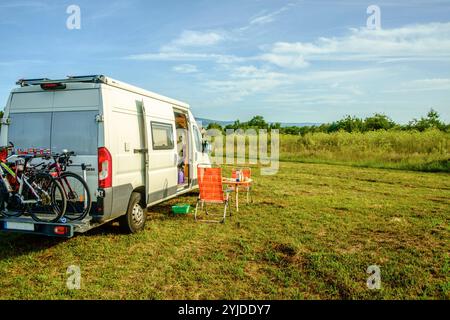 Ein Camper mit Fahrrädern am Heck steht auf einer Wiese eines Bauernhofs. Ein gedeckter Tisch und Stuhl sind vor dem Camper aufgebaut. Rhénanie-Palatinat, Deutschland. Mit einem Campervan unterwegs *** Un camping-car avec des vélos à l'arrière est garé dans un pré sur une ferme Une table et des chaises sont installées devant le camping-car Rhénanie-Palatinat, Allemagne voyageant dans un camping-car Banque D'Images