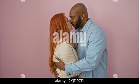 Couple interracial partageant un baiser sur un fond rose isolé, capturant l'amour et la cohésion dans un moment tendre mettant en vedette un homme et une femme. Banque D'Images