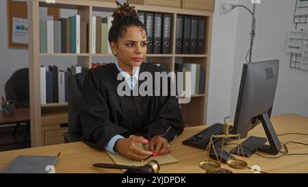 Femme juge dans le bureau travaillant à l'ordinateur portant une robe avec des livres en arrière-plan Banque D'Images