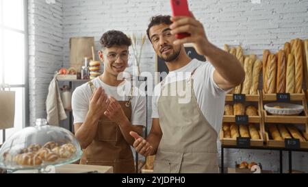 Des hommes prenant selfie dans la boulangerie, deux ouvriers hispaniques portant des tabliers souriant ensemble à l'intérieur du magasin Banque D'Images