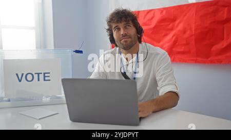 Jeune homme votant dans une salle de collège électoral en pologne avec un ordinateur portable et une boîte de vote devant un drapeau polonais Banque D'Images