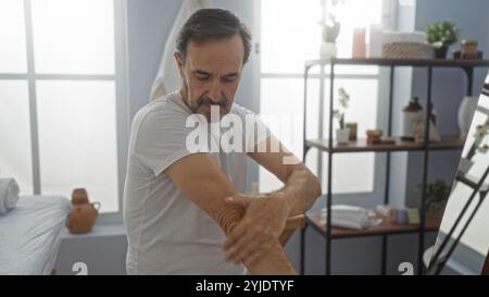 Homme hispanique mature appliquant de la crème à l'intérieur au centre de bien-être spa entouré d'un décor tranquille et d'un éclairage doux mettant l'accent sur la détente et l'auto-soin Banque D'Images