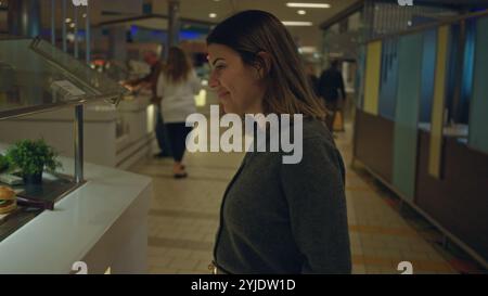 Femme souriante à l'intérieur au restaurant buffet, mettant en valeur la jeune femme hispanique appréciant la sélection de repas dans une atmosphère chaleureuse et accueillante avec une nourriture variée Banque D'Images