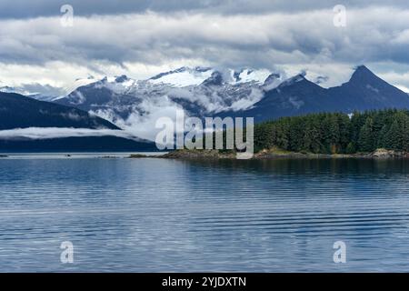 Une île forestière sur l'eau de mer calme avec un fond de montagnes enneigées en Alaska Banque D'Images