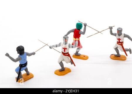 Quatre modèles miniatures en plastique Timpo chevaliers médiévaux en armure colorée s'engagent dans un combat à l'épée dynamique sur un fond blanc isolé Banque D'Images