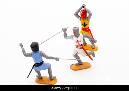 Trois modèles miniatures en plastique timpo chevaliers médiévaux en armure colorée s'engagent dans un combat à l'épée dynamique sur un fond blanc isolé Banque D'Images