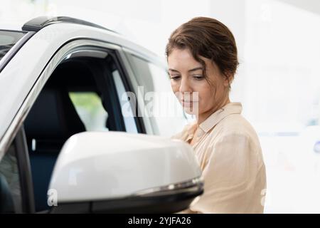 Client dans le showroom de voiture vérifiant les caractéristiques de l'automobile, comparant les modèles disponibles. Femme vérifiant la durabilité du véhicule, cherchant à prendre des décisions d'investissement éclairées, faisant l'évaluation Banque D'Images