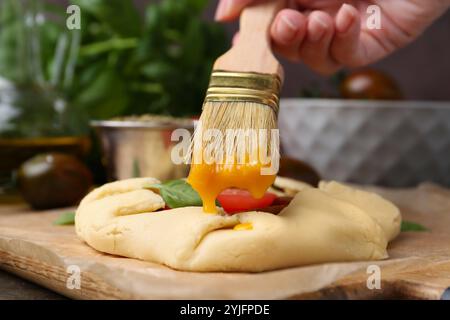 Femme mettant le jaune d'oeuf sur la galette crue avec la tomate et le basilic sur la table, gros plan Banque D'Images