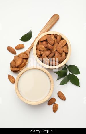 Lait de noix frais dans un bol, amandes et feuilles vertes sur une table blanche, pose à plat Banque D'Images