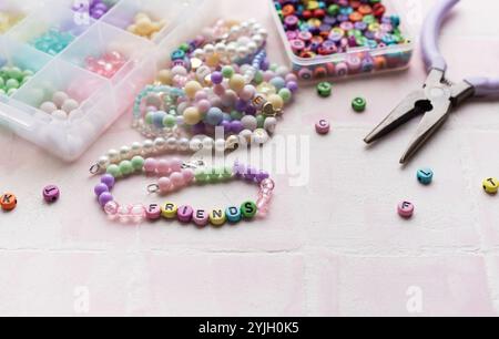 Perles colorées, perles de lettre, et pinces disposées sur un fond de tuile rose, prêt pour la fabrication de bijoux Banque D'Images