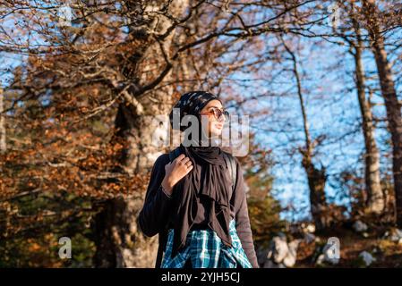 Une femme heureuse en hijab jouissant dans la nature tout en marchant dans la forêt d'automne. Banque D'Images