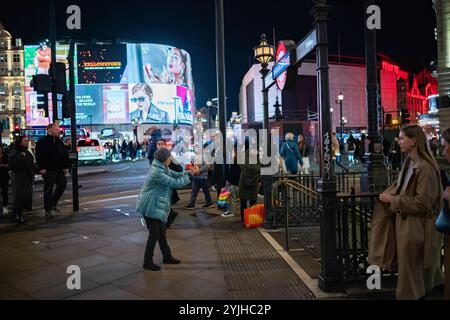 Touriste d'hiver londonien prenant des photos dans la capitale devant l'entrée de la station de métro Piccadilly Circus, West End de Londres, Angleterre, Royaume-Uni Banque D'Images