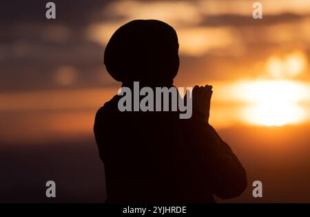 Silhouette de prière de femme musulmane ayant le culte et priant avec les mains pour remercier Dieu Allah au coucher du soleil. Banque D'Images