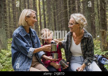 Grand-mère, mère et fille boivent du thé de thermos dans la forêt Banque D'Images