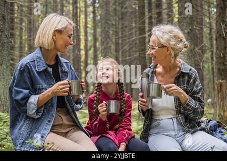 Grand-mère, mère et fille boivent du thé de thermos dans la forêt Banque D'Images