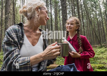 Grand-mère, mère et fille boivent du thé de thermos dans la forêt Banque D'Images