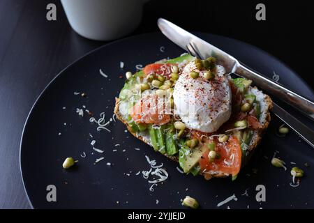 Oeufs pochés sur le dessus de l'avocat écrasé sur pain grillé au levain avec saumon fumé et germes de haricots mungo. Petit déjeuner sain avec assiette sur la table. Vue Angel. Banque D'Images