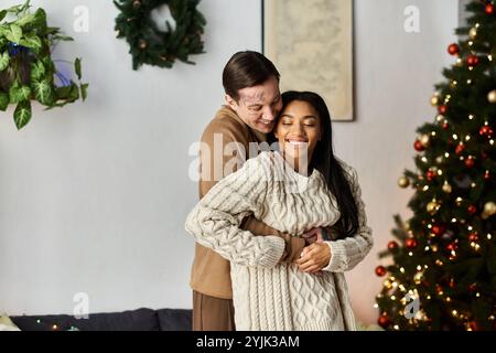 Un couple joyeux partage une étreinte chaleureuse, célébrant l'amour de Noël ensemble à la maison. Banque D'Images