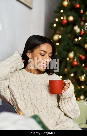 Un moment chaleureux alors qu'une femme profite d'une atmosphère festive de vacances près du sapin de Noël. Banque D'Images