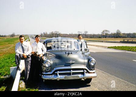 Trois hommes en costumes d'affaires se tiennent par Oldsmobile 88 voiture sur la route de l'autoroute, USA c 1953 Banque D'Images