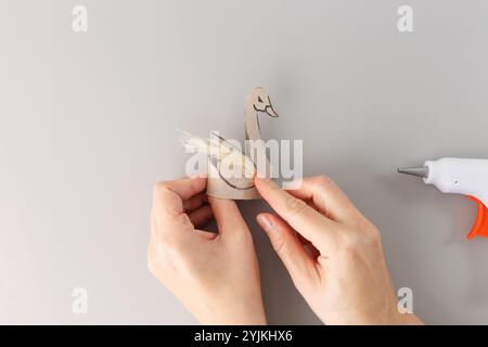 Vue de haut en bas, mains fabriquant la figurine de cygne à partir de carton et d'herbe de pampa à l'aide d'un pistolet à colle chaude sur un fond gris. Concept DIY. tutoriel, blog artisanal Banque D'Images