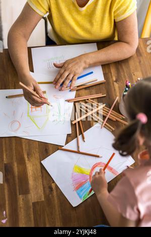 Vue de dessus d'une charmante fille et sa grand-mère dessinant joyeusement dans un album avec des stylos colorés. Photo de haute qualité Banque D'Images