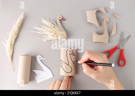 un projet d'artisanat créatif en cours. une main tient un crayon et dessine le contour du cygne sur un rouleau de carton cylindrique. derrière, il y a prêt Banque D'Images