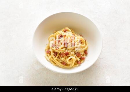 Plat de pâtes italiennes avec pancetta croustillante, fromage parmesan et poivre noir dans un bol en céramique blanche sur fond clair. Vue rapprochée Banque D'Images