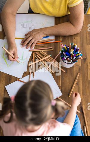 Vue de dessus d'une charmante fille et sa grand-mère dessinant joyeusement dans un album avec des stylos colorés. Photo de haute qualité Banque D'Images